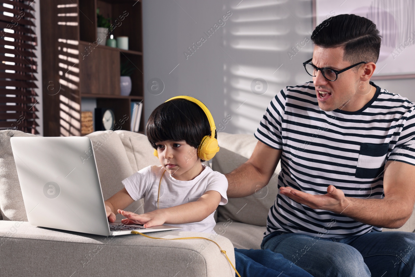 Photo of Internet addiction. Man scolding his son while he using laptop in living room