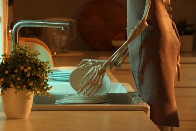 Photo of Human skeleton washing dishes in kitchen sink at night, closeup