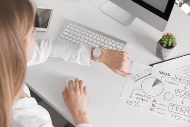 Photo of Young woman checking time on her wristwatch at workplace