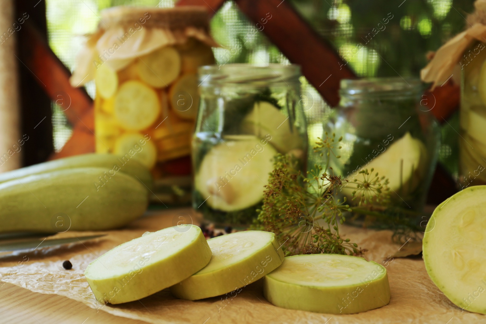 Photo of Cut fresh zucchini and jars of pickled vegetables on white wooden table, closeup