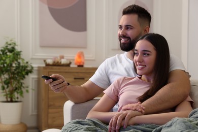 Happy young couple watching tv on sofa in living room. Space for text