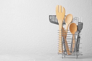 Photo of Set of kitchen utensils in stand on stone table near light wall. Space for text
