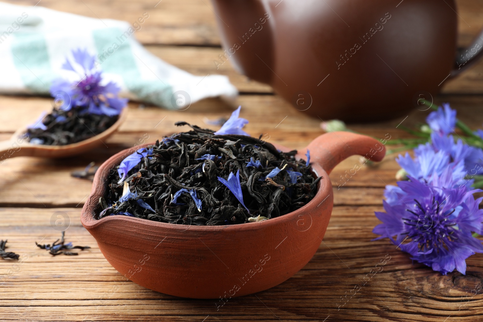 Photo of Dry tea leaves and cornflowers on wooden table, closeup