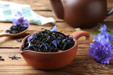 Photo of Dry tea leaves and cornflowers on wooden table, closeup