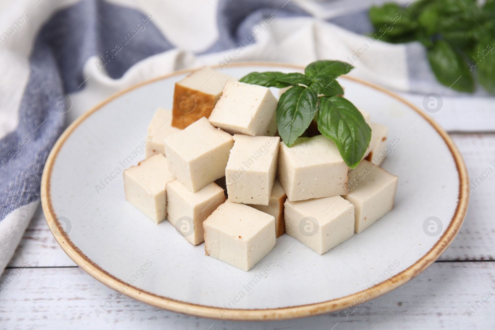 Photo of Plate with delicious smoked tofu and basil on white wooden table, closeup