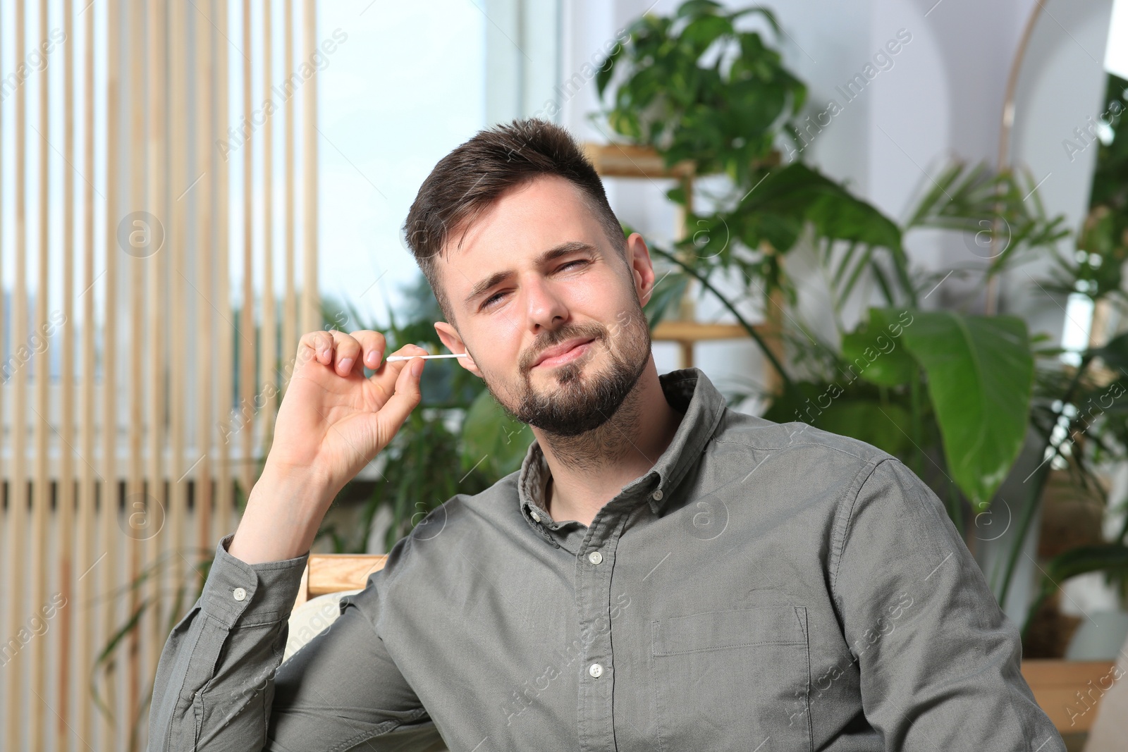 Photo of Young man cleaning ear with cotton swab at home