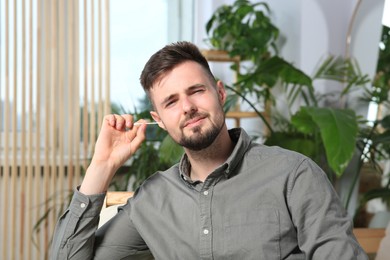 Photo of Young man cleaning ear with cotton swab at home