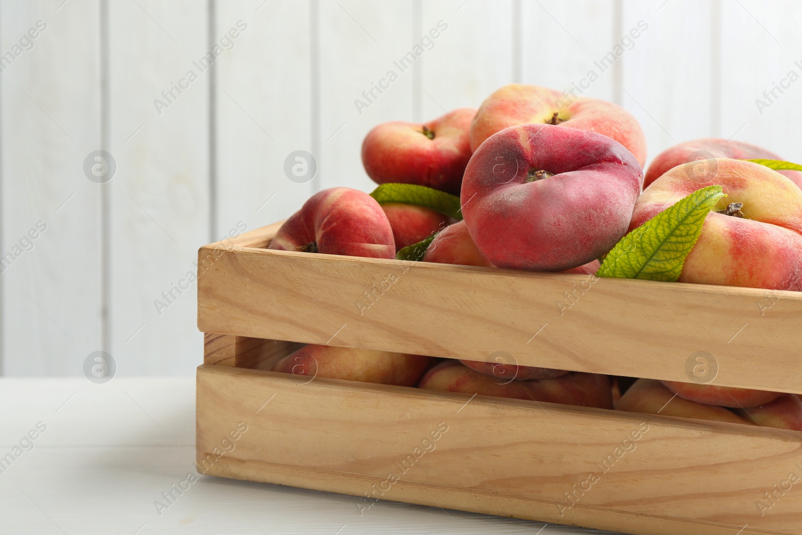 Photo of Fresh ripe donut peaches in crate on white wooden table