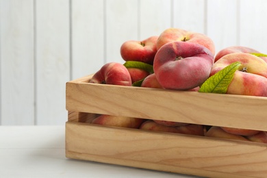 Photo of Fresh ripe donut peaches in crate on white wooden table