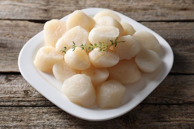 Photo of Fresh raw scallops and thyme on wooden table, closeup