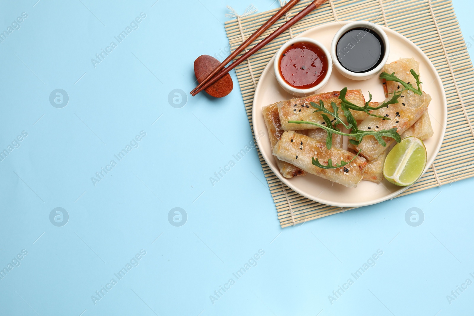 Photo of Tasty fried spring rolls served on light blue table, flat lay. Space for text