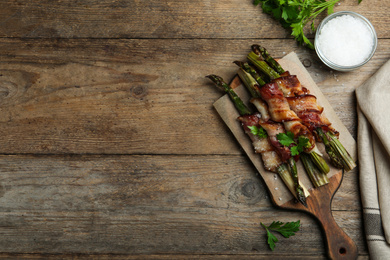 Photo of Oven baked asparagus wrapped with bacon on wooden table, flat lay. Space for text