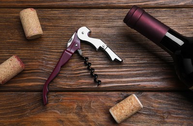 Corkscrew, wine bottle and stoppers on wooden table, flat lay