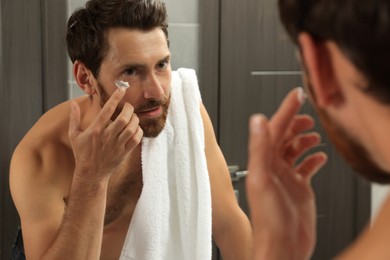 Photo of Handsome man applying cream on face in bathroom near mirror