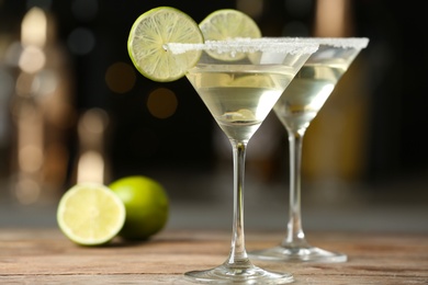 Photo of Glasses of Lime Drop Martini cocktail on wooden table against blurred background