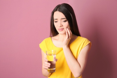 Woman with sensitive teeth holding glass of water on color background