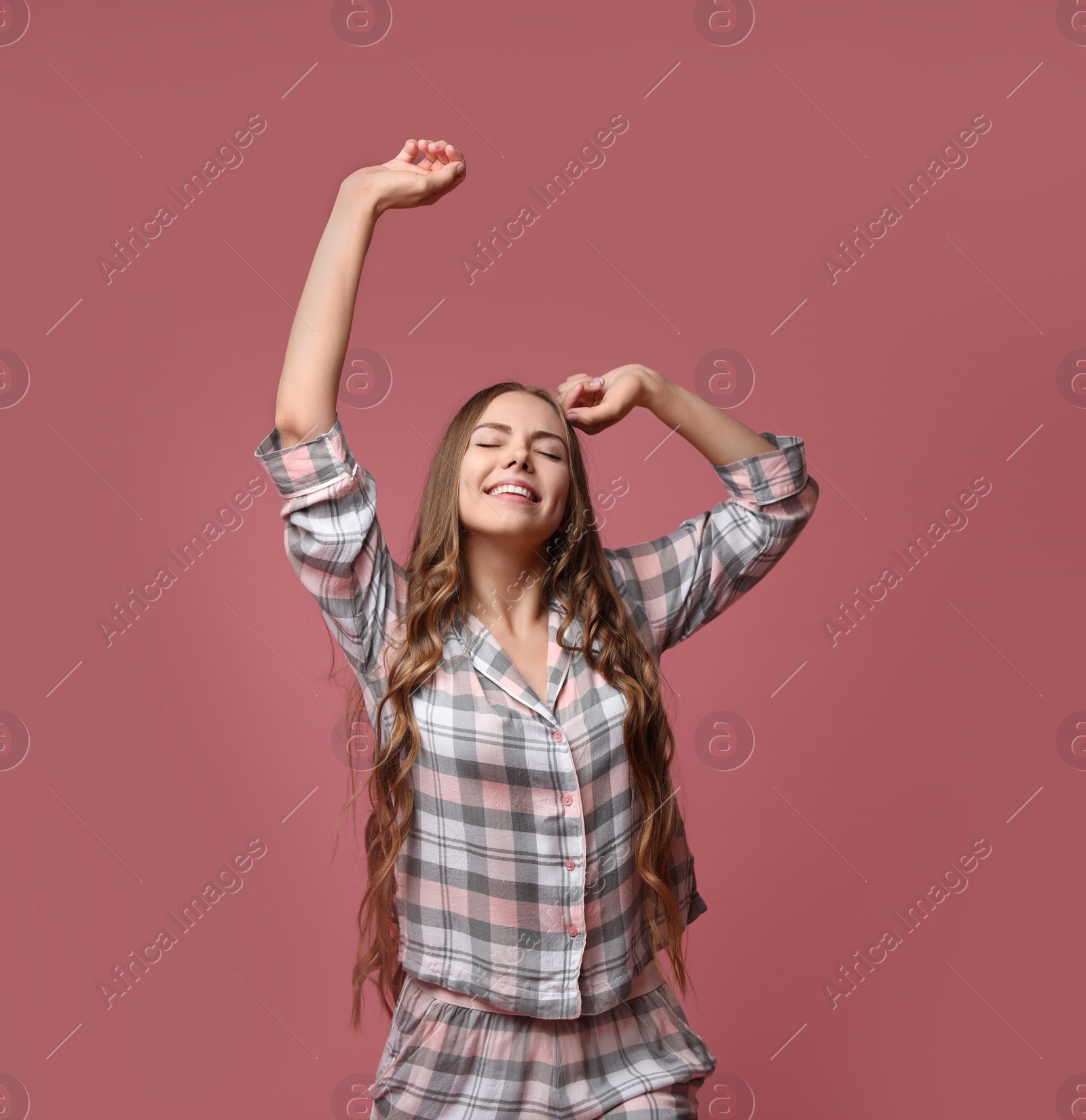 Photo of Beautiful woman in pajamas stretching on dusty rose background. Bedtime