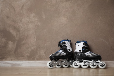 Photo of Inline roller skates on floor near brown wall. Space for text