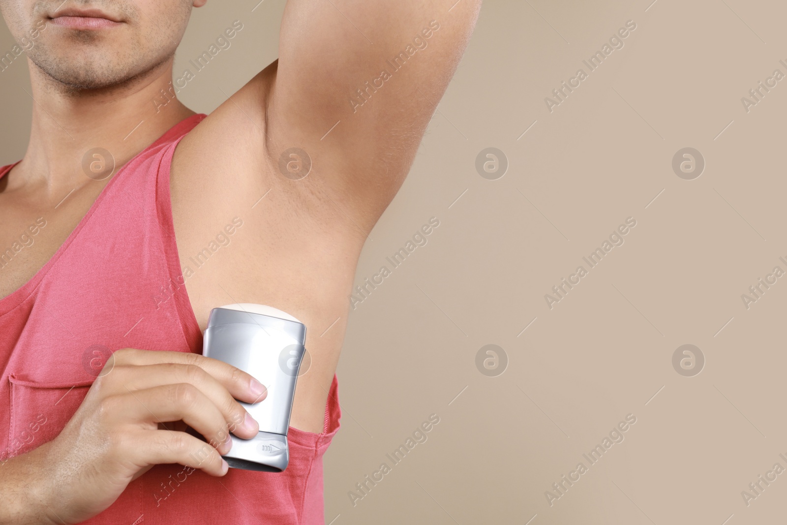 Photo of Young man applying deodorant to armpit on beige background, closeup. Mockup for design