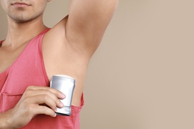 Photo of Young man applying deodorant to armpit on beige background, closeup. Mockup for design