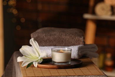 Photo of Spa composition with burning candle, lily flower and towels on massage table in wellness center