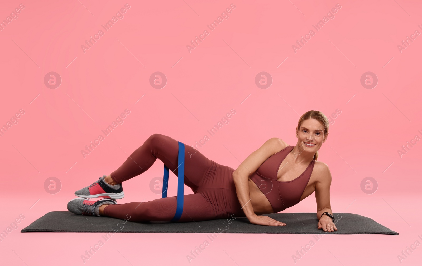 Photo of Woman exercising with elastic resistance band on fitness mat against pink background