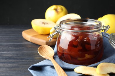 Quince jam in glass jar, spoon and fresh raw fruits on grey table, closeup. Space for text