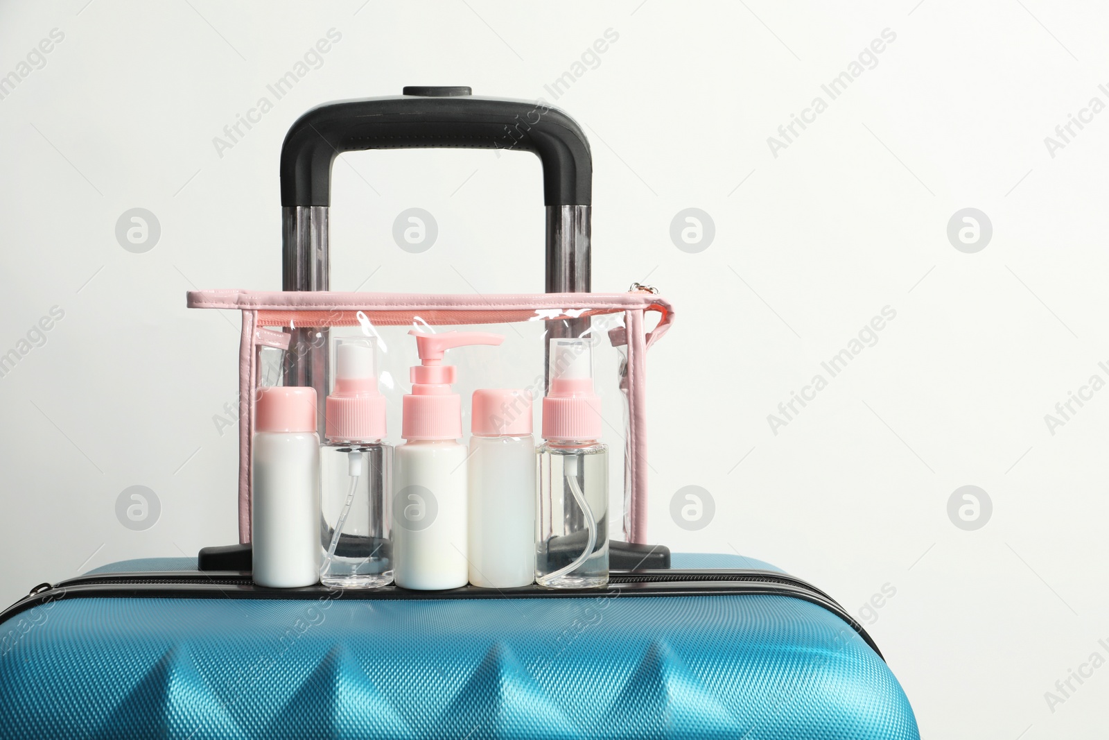 Photo of Cosmetic travel kit in plastic bag on suitcase against light background, space for text