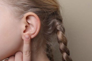 Photo of Cute little girl pointing at her ear on beige background, closeup