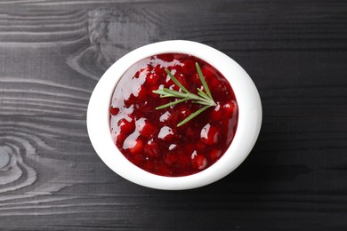 Photo of Fresh cranberry sauce in bowl and rosemary on black wooden table, top view