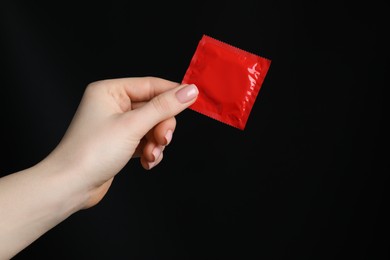 Photo of Woman holding condom on black background, closeup