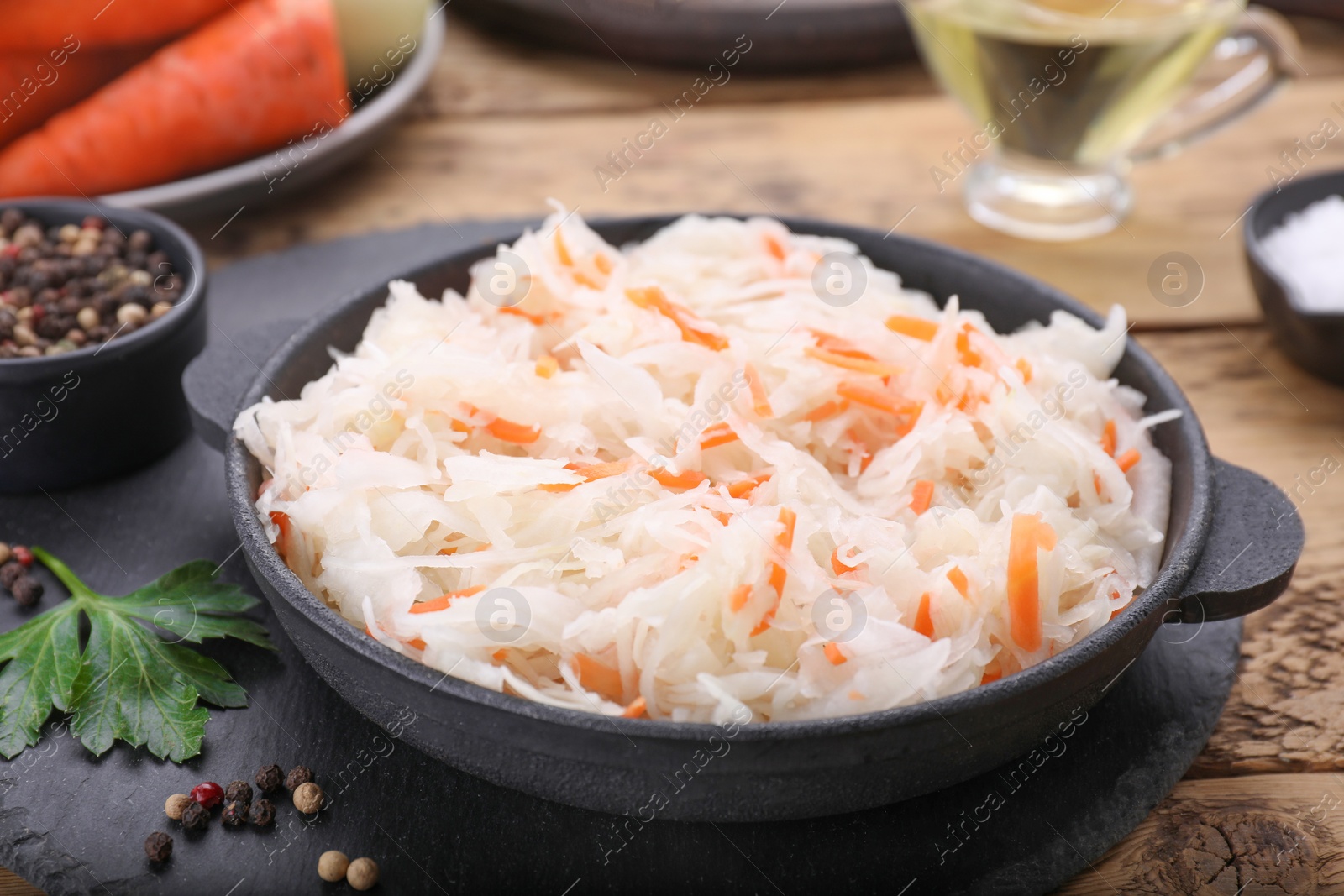 Photo of Bowl of tasty sauerkraut and ingredients on wooden table, closeup