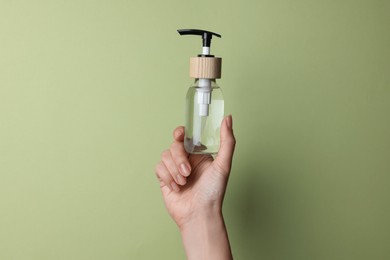 Photo of Woman holding bottle of cosmetic product on pale olive background, closeup. Space for text