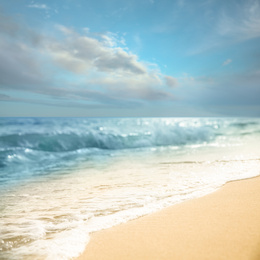 Image of Ocean waves rolling on sandy beach under blue sky with clouds