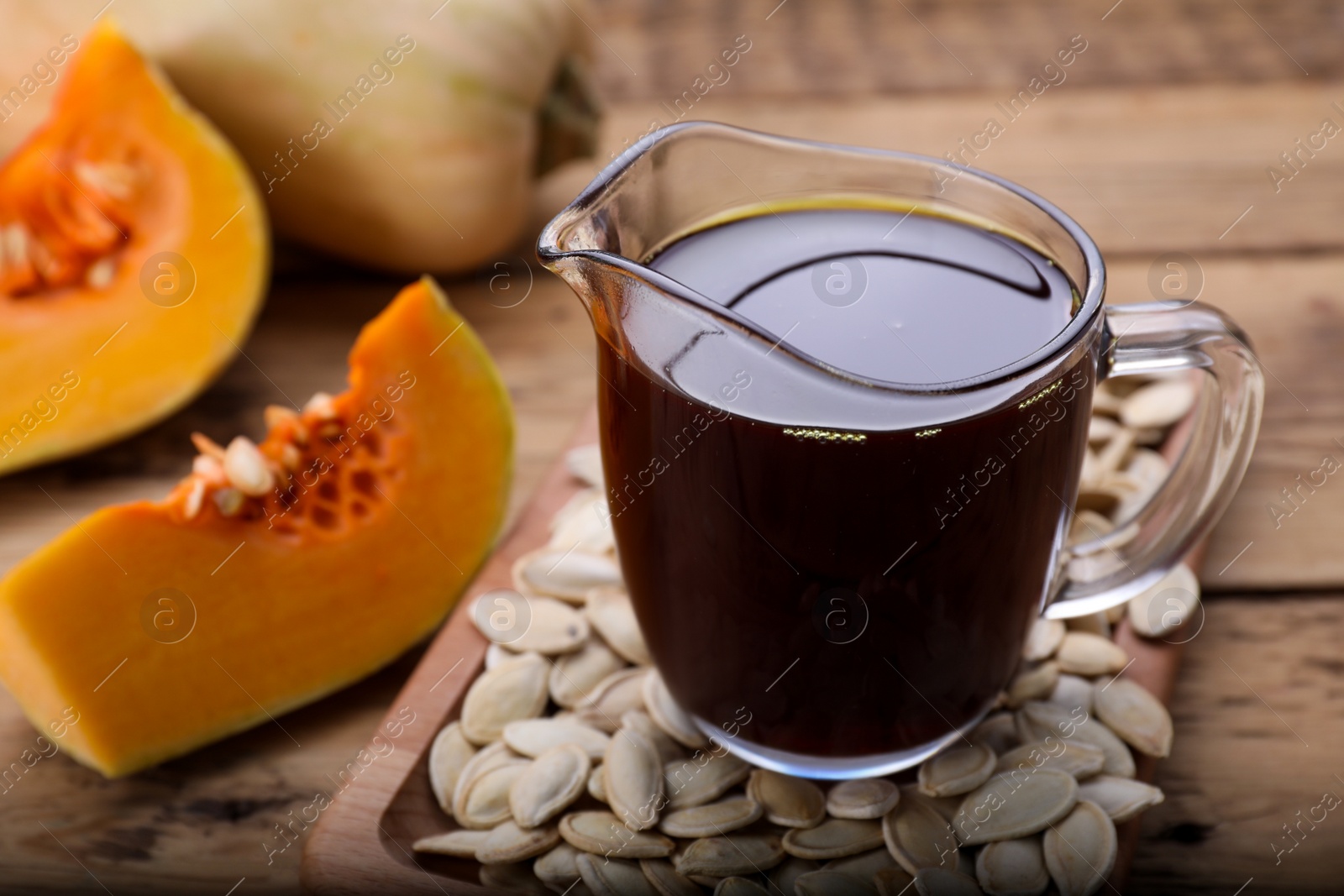 Photo of Fresh pumpkin seed oil in glass pitcher on wooden table