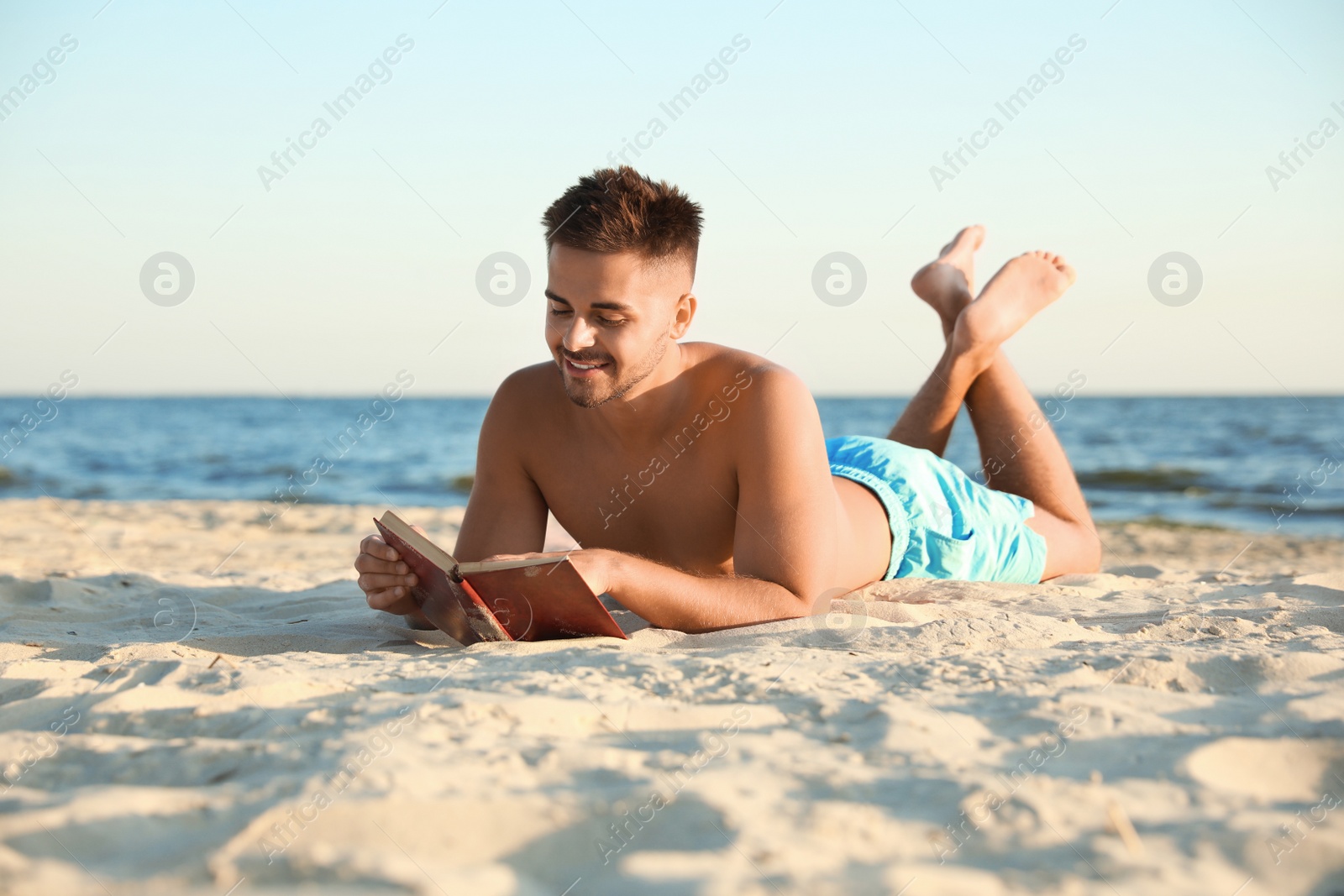 Photo of Young man reading book on sandy beach near sea