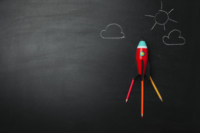 Photo of Bright toy rocket, school supplies and drawings on chalkboard, flat lay. Space for text