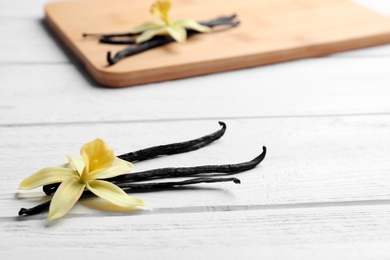 Photo of Vanilla sticks and flowers on wooden background, closeup. Space for text
