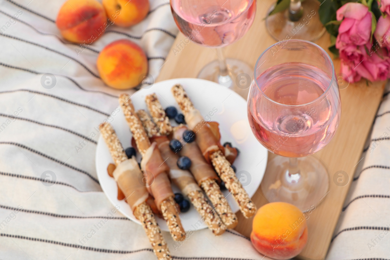 Photo of Glasses of delicious rose wine, flowers and food on white picnic blanket