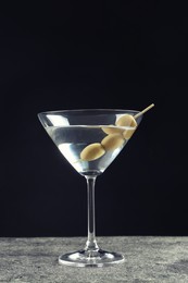 Martini cocktail with olives on grey table against dark background
