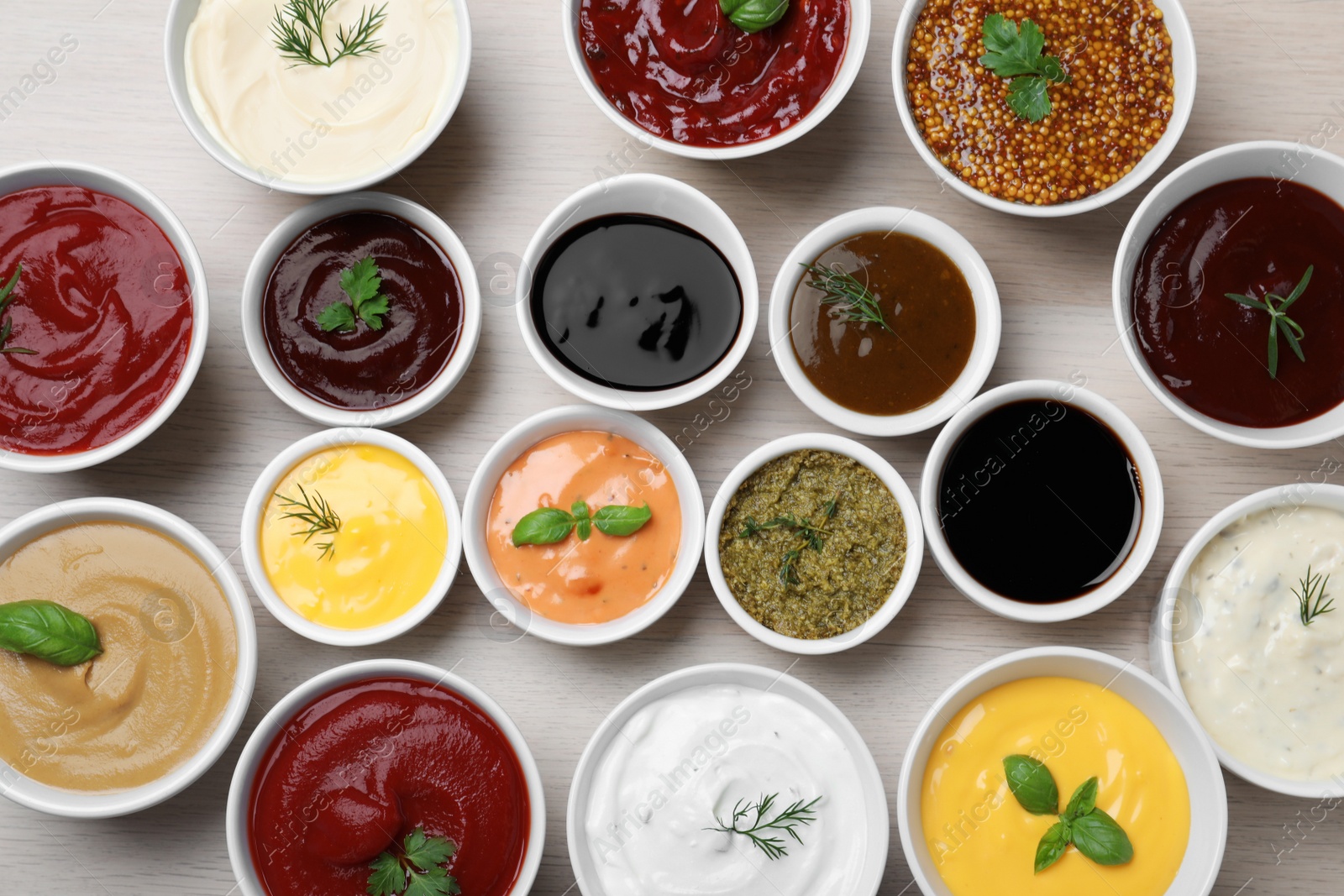 Photo of Many bowls with different sauces and herbs on wooden table