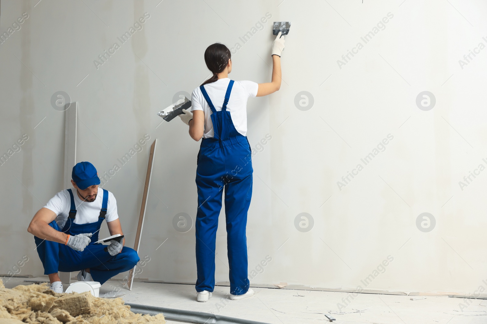 Photo of Professional workers plastering wall with putty knives indoors