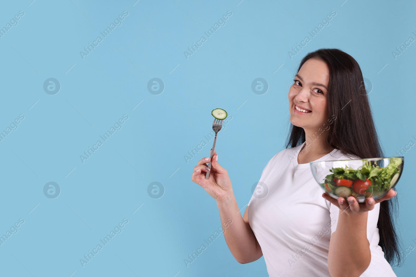 Photo of Beautiful overweight woman eating salad on light blue background, space for text. Healthy diet