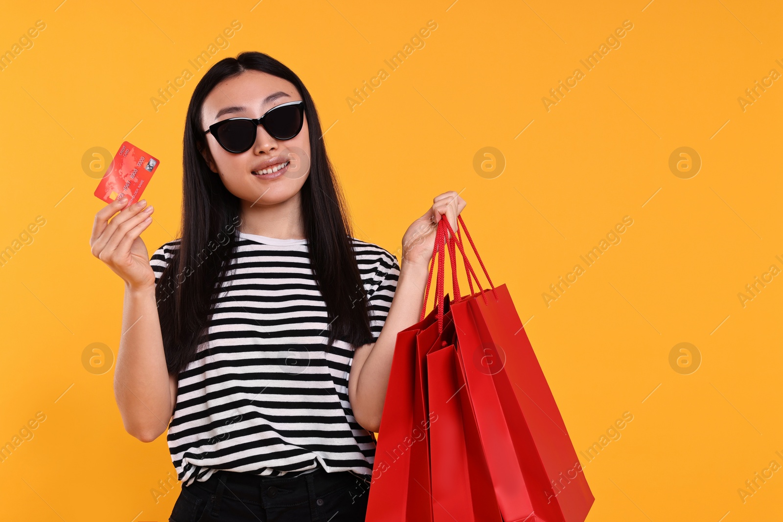 Photo of Happy woman with shopping bags and credit card on yellow background. Space for text