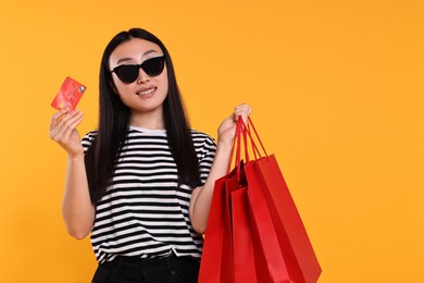 Happy woman with shopping bags and credit card on yellow background. Space for text