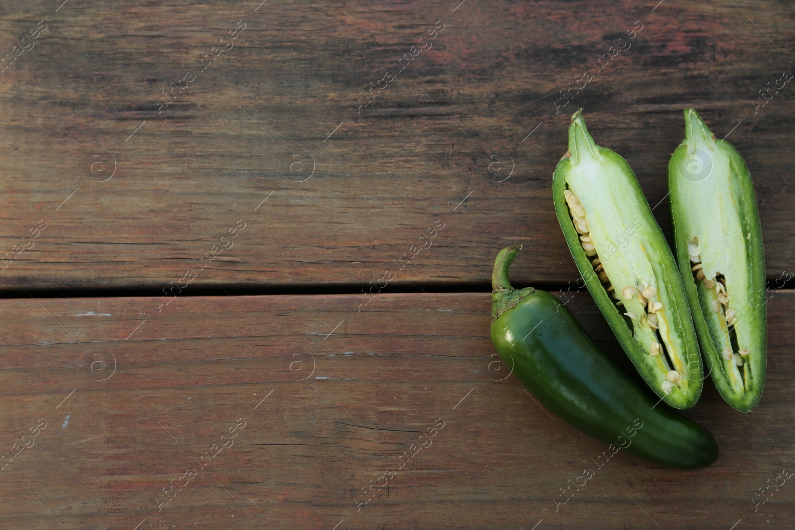 Photo of Whole and cut green chili peppers on wooden table, flat lay. Space for text