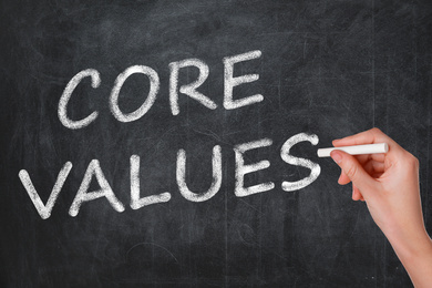 Woman writing phrase CORE VALUES on blackboard, closeup