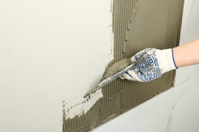 Closeup of worker spreading concrete on wall with spatula, space for text. Tile installation