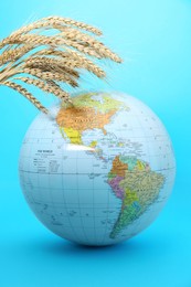 Photo of Globe with wheat spikelets on turquoise background. Hunger crisis concept