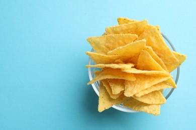 Photo of Tortilla chips (nachos) in glass bowl on light blue background, top view. Space for text
